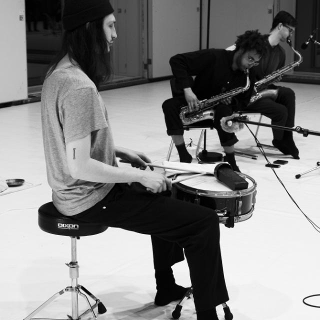 A photo of Paul Amereller playing the snare drum, and Tapiwa Svosve and Tobias Pfister playing the saxophone